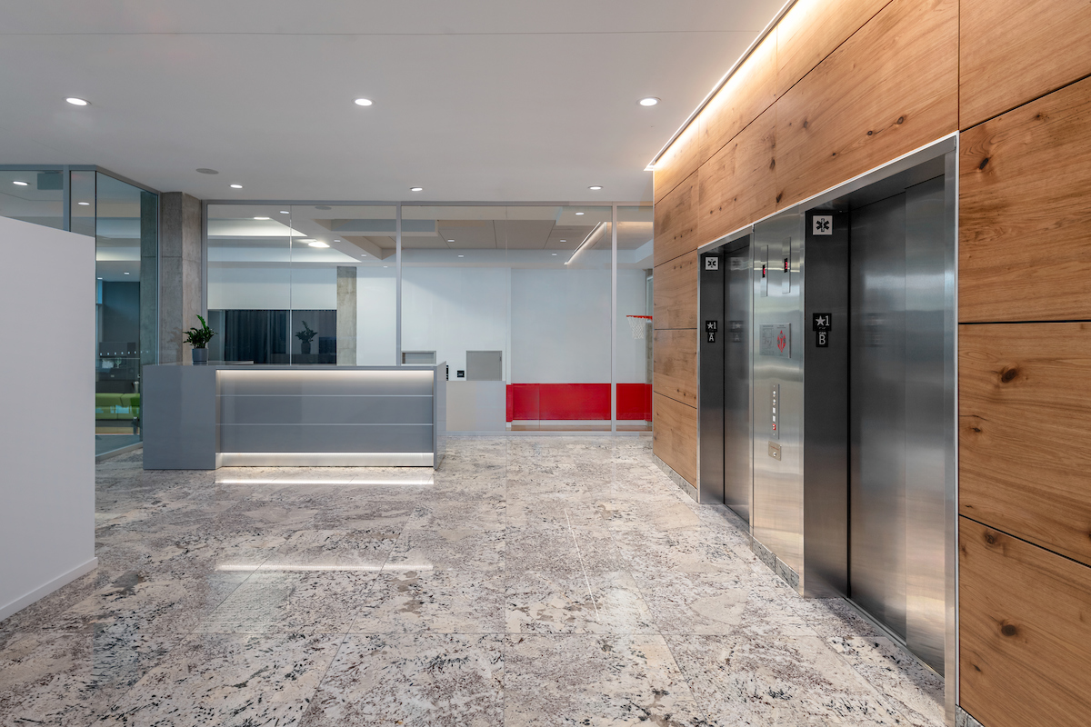 Modern office lobby with marble floors, wooden wall panels, a reception desk, and two stainless steel elevators for optimized service.