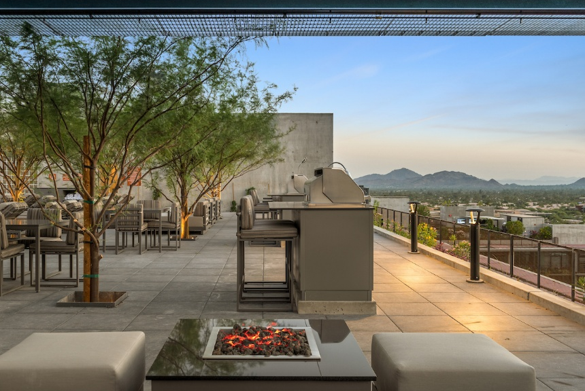 Stylish Sky Deck rooftop patio with seating, fire pit, grill, trees, and scenic mountain views—perfect for memorable evenings at sunset.