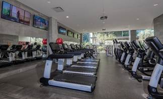 A modern gym with treadmills, exercise bikes, large mirrors, red exercise balls, and TVs on the wall.