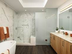 Modern bathroom with a glass shower, freestanding tub, wooden cabinets, and marble walls. Orange towels and plants decorate the space.