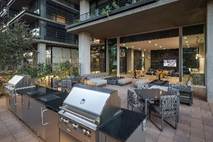 Outdoor patio with stainless steel grills and lounge seating, perfect for easy wellness gatherings by a modern building with large windows.