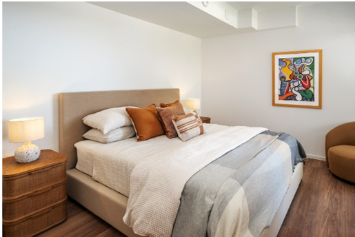 Modern bedroom with beige bed, layered pillows, and abstract art—showcasing common features of the Optima Portfolio living experience.